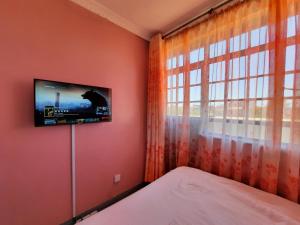 a bedroom with a tv on the wall next to a window at Pine Residency w Secure Parking, Wifi, Netflix & Rooftop Views in Kikuyu