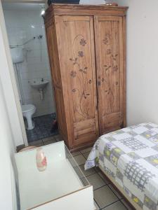 a bedroom with a bed and a wooden cabinet and a bathroom at Pituba quartos in Salvador