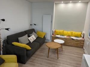 a living room with a black couch and yellow pillows at Bel appartement plein centre 100m de la mer in Merville-Franceville-Plage