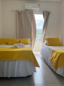 two beds with yellow sheets in a room with a window at Pousada Suites Enseada Guaruja in Guarujá
