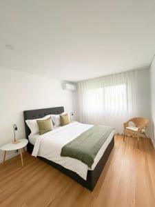 a white bedroom with a large bed and a chair at Ri&Vale Alojamentos in Vieira do Minho