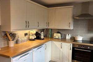 cocina con armarios blancos y encimera de madera en Cosy 2 bed, home from home en Haddenham