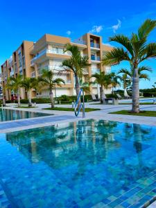 a swimming pool in front of a building with palm trees at Apartamento frente a Playa in San Pedro de Macorís