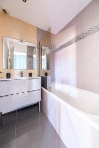 La salle de bains est pourvue d'une baignoire, d'un lavabo et de miroirs. dans l'établissement Confort Golf Disney, à Bailly-Romainvilliers