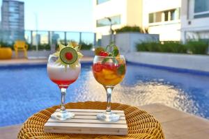 two glasses of drinks on a table next to a pool at Quarto para 4 pessoas in Campos dos Goytacazes