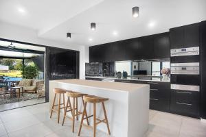 a kitchen with black cabinets and a white counter with stools at Executive, modern waterfront house in Maroochydore