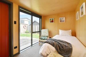 a bedroom with a bed and a sliding glass door at Beachfront Bach - Christchurch Holiday Homes in Christchurch