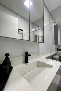 a white bathroom with a sink and a mirror at Studio de frente para o mar em Balneário Camboriú in Balneário Camboriú