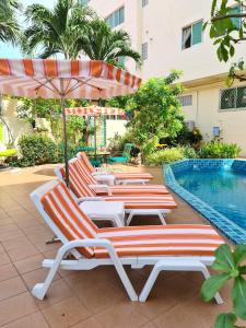 four lounge chairs and an umbrella next to a swimming pool at BUTTERFLY GARDEN BOUTIQUE RESIDENCE by Luxury View EX LG Apts and Villas, A Lifestyle Destination 1 to 3 bedroom units 110 to 190 sqmtr, 2 FULL Bathrooms, Rain shower, Complete kitchen, FREE Fast Fiber WIFI, 55" SMART TVs, 24-7 Staff, SPA BATH, FREE BBQ in Pattaya South