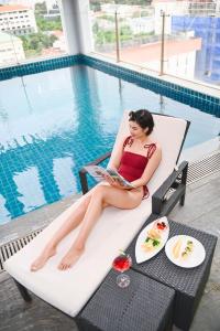 ホーチミン・シティにあるMuong Thanh Grand Saigon Centre Hotelの椅子に座ってプールサイドで本を読む女性