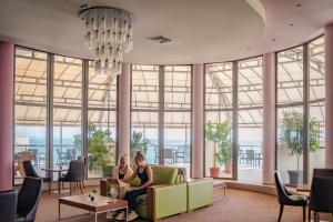 Dos mujeres sentadas en un sofá en una habitación con ventanas grandes en Golden Beach Park Hotel - All inclusive, en Golden Sands
