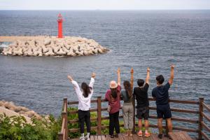 eine Gruppe von Menschen, die auf einem Pier stehen und einen Leuchtturm ansehen in der Unterkunft Bedradio Dodubong in Jeju-do