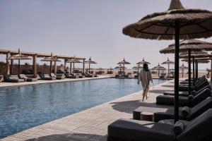 a woman walking by a swimming pool with chairs and umbrellas at Casa Cook El Gouna - Adults Only in Hurghada