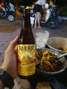a person holding a bottle of beer next to a bowl of food at Môn Bạc Home in Da Lat