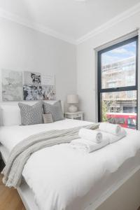 a white bedroom with a large white bed with a window at Pleasing 2bed flat 10min to Wimbledon tennis court in London