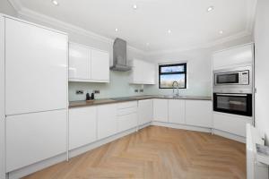 cocina blanca con armarios blancos y suelo de madera en 3bed Penthouse 10min to Wimbledon tennis courts, en Londres