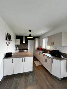 a kitchen with white cabinets and a wooden floor at Maison 3 ch vue sur mer confortable lumineuse belle terrasse grand jardin 10 mn à pied de la plage - proche supérette et Omaha Beach in Vierville-sur-Mer