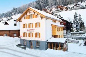 a building with snow on the ground next to a mountain at Boardercamp Laax - swiss mountain hostel in Ruschein