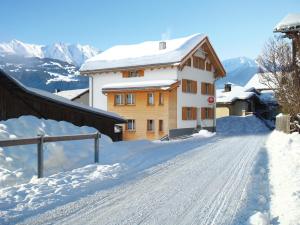 una carretera cubierta de nieve con un edificio en el fondo en Boardercamp Laax - swiss mountain hostel, en Ruschein