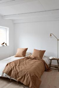 a white bedroom with a bed with brown sheets at Gartnerhuset på Kollerup in Hadsten Stationsby