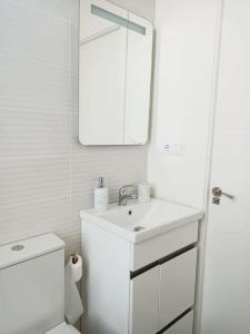 een witte badkamer met een wastafel en een spiegel bij Herba de namorar- Céntrico apartamento en Cedeira in Cedeira