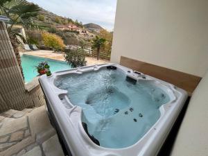 a bath tub on a balcony with a swimming pool at Chambre au calme avec spa privatif gratuit sud aveyron les palmiers des causses in Saint-Rome-de-Tarn