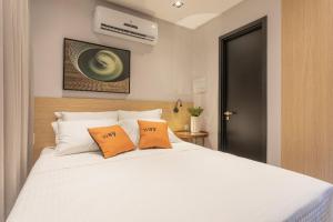 1 dormitorio con 1 cama blanca y 2 almohadas de color naranja en Way Bossa #C2 - Flat Praia do Bessa by Carpediem, en João Pessoa