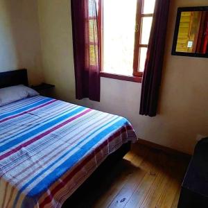 1 dormitorio con 1 cama con edredón a rayas y ventana en Chalés Rota do Sol Praia do Rosa, en Praia do Rosa