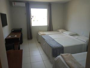 a room with two beds and a desk and a window at Quarto139 Portobello Park in Porto Seguro