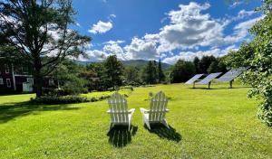 two white chairs sitting in the grass in a field at The Griff Inn in Waitsfield