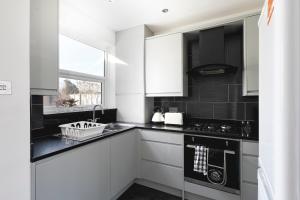 una cocina con armarios blancos y encimeras negras en Skyvillion - London Enfield 4 Bedroom Lush House Free Parking Garden, en Enfield Lock