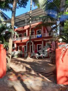 a red building with palm trees in front of it at Cherry blossom guest house in Arpora