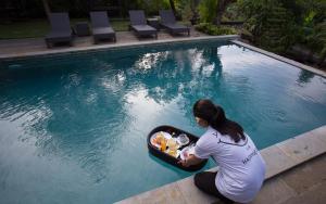 a woman sitting next to a pool with a tray of food at Klumpu Hill Villas Nusa Penida in Nusa Penida +36 photos