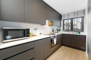 uma cozinha com armários cinzentos e um micro-ondas em Modern 4 Bedroom House With Parking in Farnham Royal, Slough By Ferndale em Slough