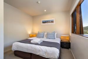 Un dormitorio con una cama con almohadas azules y una ventana en Snow Stream 2 Bedroom and loft with gas fire balcony and garage parking, en Thredbo