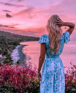 Una mujer con un vestido azul mirando al océano en Waenis Sunset View Hotel and Restaurant, Amed, Bali, en Amed