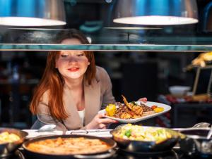a woman is holding a plate of food at Centro Capital Doha - By Rotana in Doha
