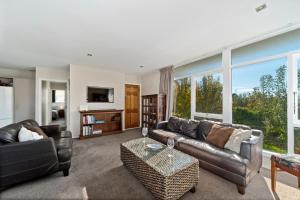 a living room with leather furniture and a large window at The Orchard House - Turangi Holiday Home in Turangi