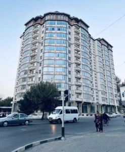 a large building with cars parked in front of it at Апартамент в центре города Худжанд in Khujand