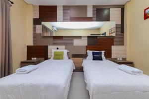 2 bedden in een hotelkamer met witte lakens bij Urbanview Hotel WG Jimbaran Bali in Ungasan