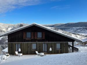 een groot houten huis in de sneeuw met stoelen bij La maison de Cécile in Ventron