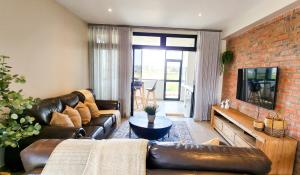 a living room with a leather couch and a brick wall at Kabeljauws Beach Apartments in Jeffreys Bay
