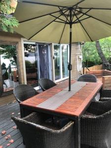 une table en bois avec des chaises et un parasol sur une terrasse dans l'établissement Om chalet 2 avec spa et foyer bordé du fleuve, à Saint-Pierre-de-l'Île-d'Orléans