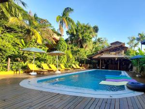 uma piscina com cadeiras e guarda-sóis num deque de madeira em Hotel Pousada Katmandu em Maresias