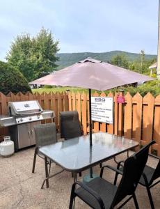 einen Tisch und Stühle mit einem Sonnenschirm und einem Grill in der Unterkunft Loft LèSKImo, lit king, sauna, piscine et montagne in Saint-Férréol-les-Neiges