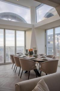 uma sala de jantar com mesa, cadeiras e janelas em Penthouse Royal, Luxurious and cozy with Sauna em Cadzand
