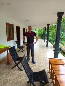 un hombre parado en un porche con dos sillas en Hotel Chanaya en Ambanpola