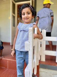 una niñita parada junto a una valla de madera en Hiddenvalley Stays - Nethra, en Madikeri