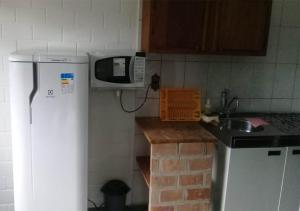 a kitchen with a microwave and a sink and a refrigerator at Vila da Praia in Boicucanga