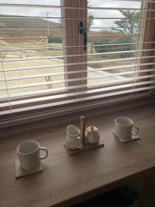 duas xícaras e pires sentados numa mesa ao lado de uma janela em Dolmen Lodge. em Donegal